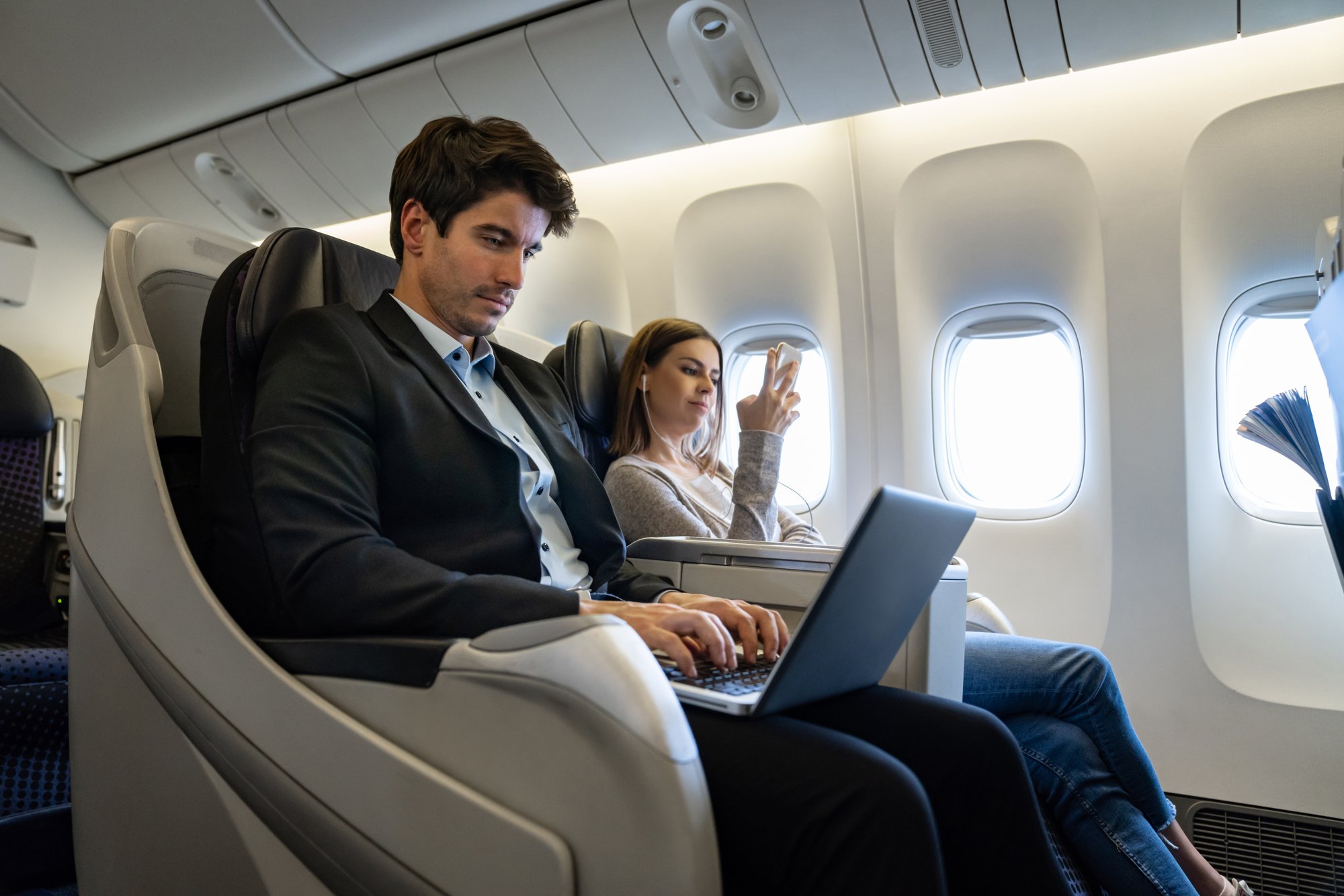 Passengers in business class seating; man using a laptop, woman holding a smartphone