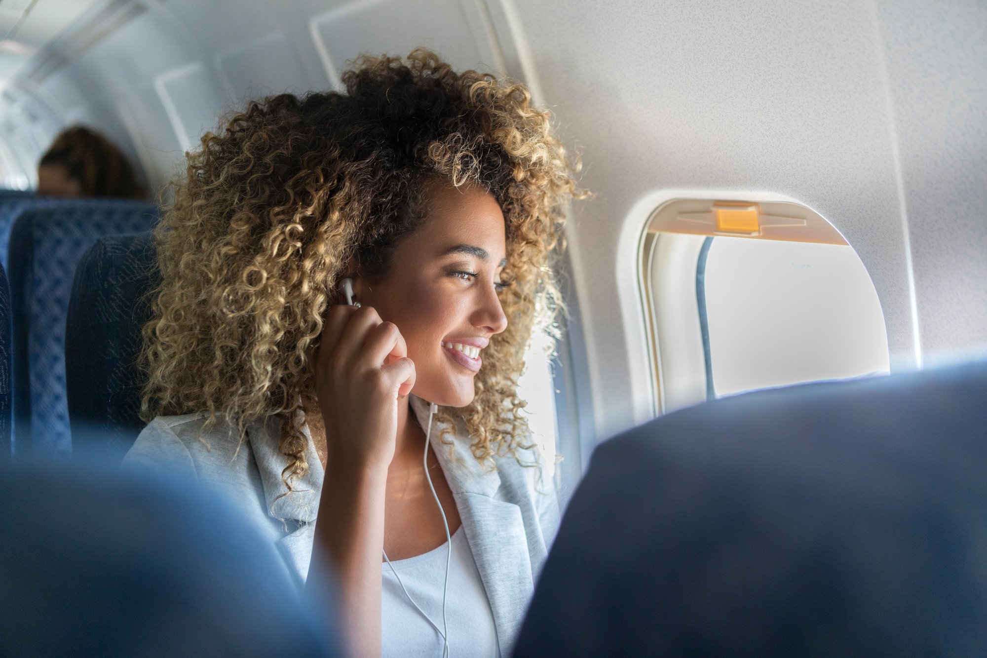 Woman with curly hair smiling while listening to earphones on an airplane