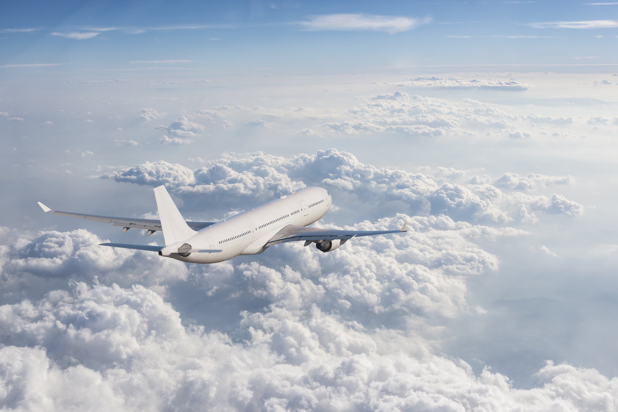 Airplane flying above a bed of fluffy clouds with a blue sky in the background