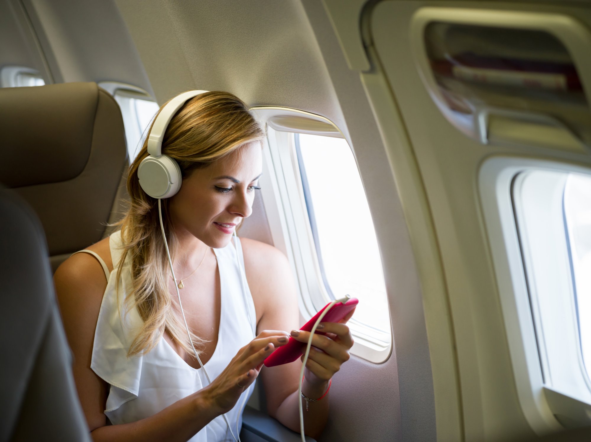 Woman wearing headphones using a smartphone on an airplane