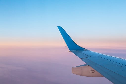 View of an airplane wing with a pastel gradient sky from pink to blue in the background