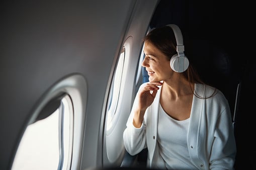 Smiling woman with headphones looking out an airplane window.