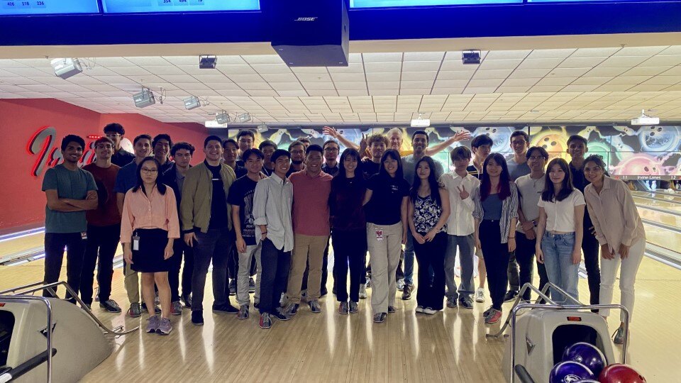 A group of about 23 people posing on bowling lanes inside a bowling alley