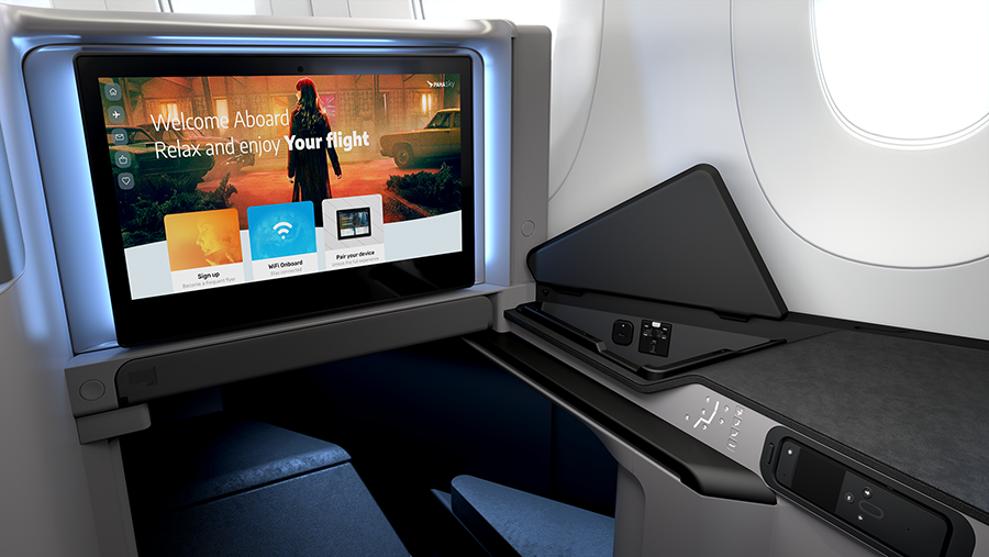 First-class airplane suite with a large entertainment screen displaying welcome message and menu options